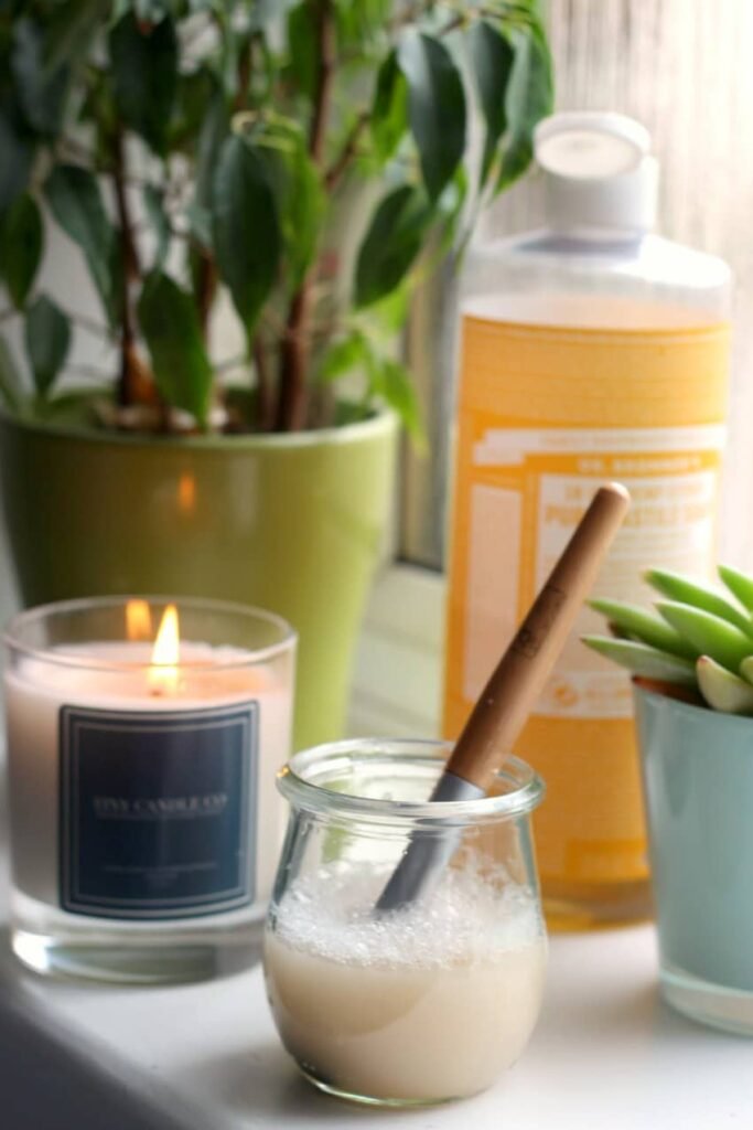 cosmetics brush sitting in a jar of homemade makeup brush cleaner, next to a bottle of liquid castile soap.