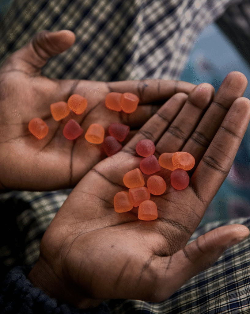 Two hands holding several small, orange and red gummy candies against a plaid fabric background.