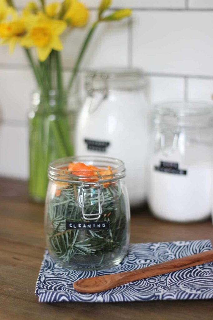 Jar of pine infused cleaner on a wooden work surface, next to a blue and white tea towel and wooden spoon.
