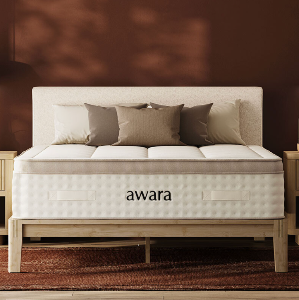 5 Best Mattresses For Hot Sleepers (2026) A bed with a beige headboard, neutral pillows, and an "awara" branded mattress sits between two wooden nightstands against a brown wall.