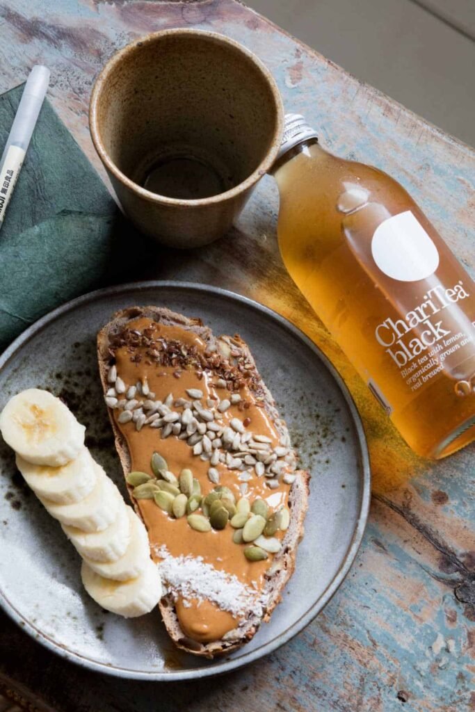 Bottle of Charitea's ethical soft drinks next to a slice of bread with peanut butter, seeds, and sliced bananas.