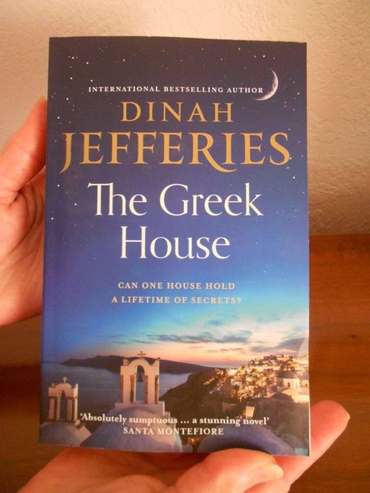 Secrets and Betrayal in The Greek House by Dinah Jefferies My hand holding The Greek House by Dinah Jefferies book.