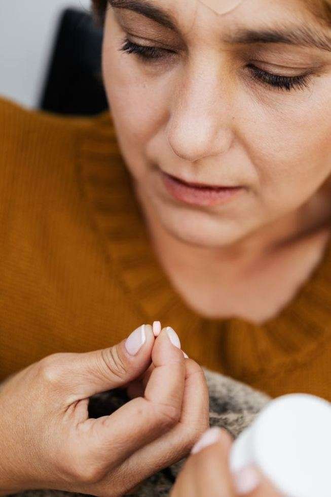 Antihistamines and Dementia Risk: What You Should Know About Allergy Meds Woman in an orange sweater holding a small allergy pill while reading an antihistamines container label for dementia risk.